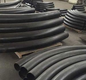 Large black metal pipes bent into curves, neatly stacked on wooden pallets in an industrial setting.